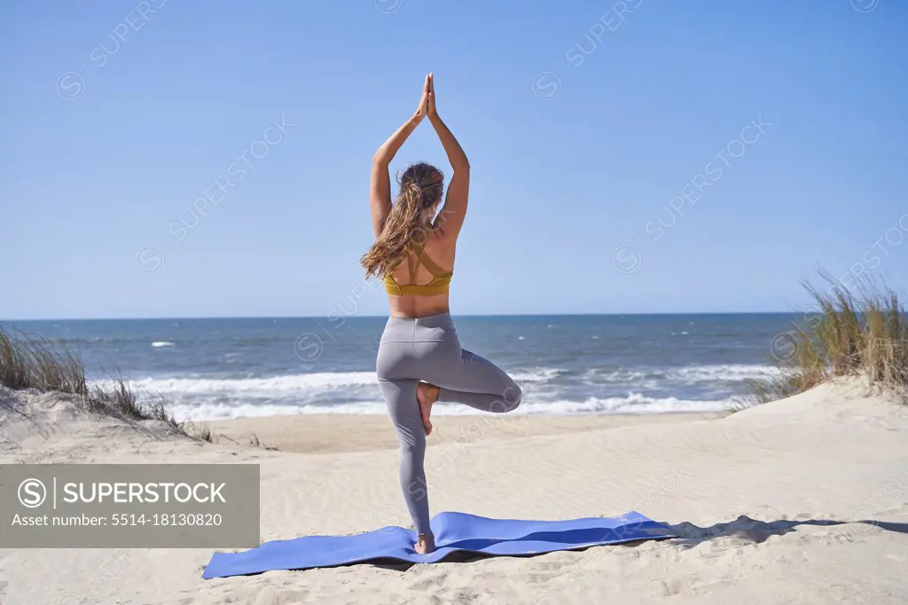 Concentrated young girl does Vrikshasana pose on the beach in the morning. Girl doing a handstand.