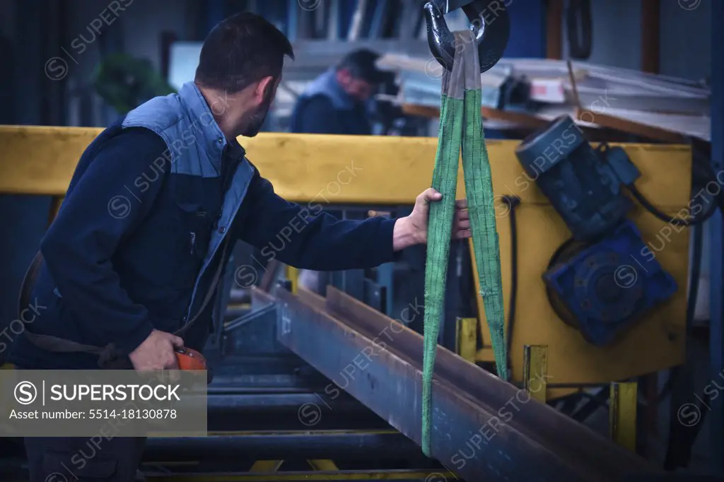 Man putting steel beam on cutting machine with crane
