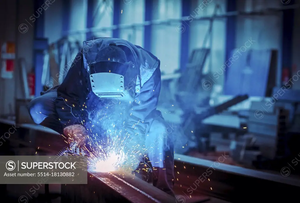 Man with protective face and eye shield welding industrial steel beam