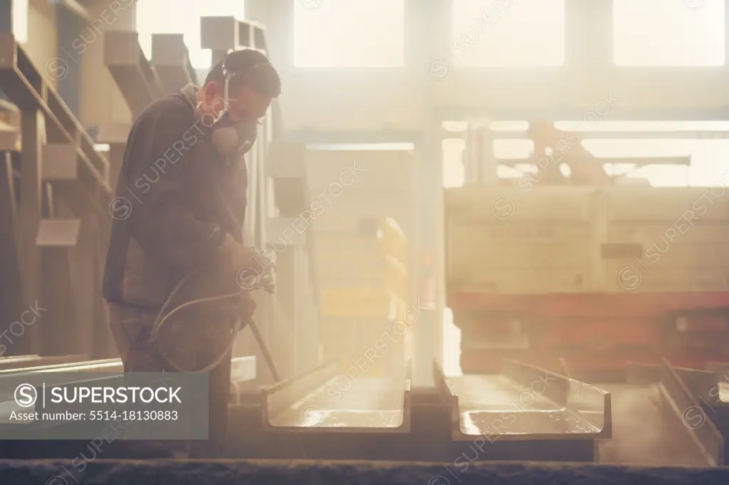 Man painting industrial and lacquering steel with compressor machine