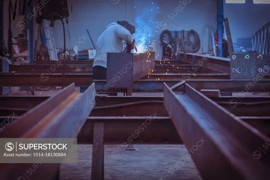 Man with protective face and eye shield welding industrial steel beam