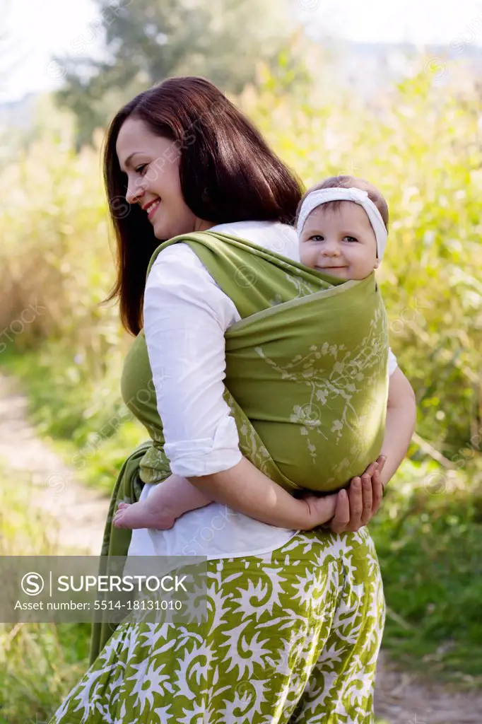 Happy smiling family with mom and girl back in green sling carrier