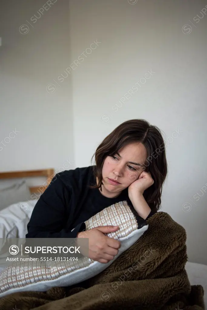 Woman sitting in bed resting head on hand looking distant