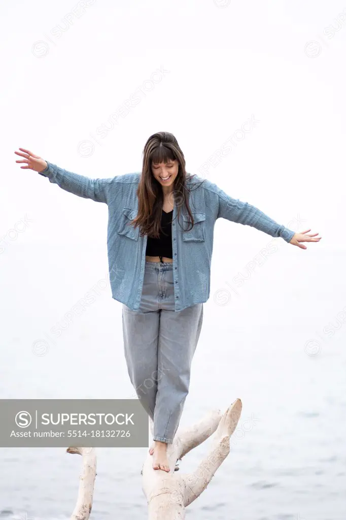 young woman standing on white wooden log with sea in background