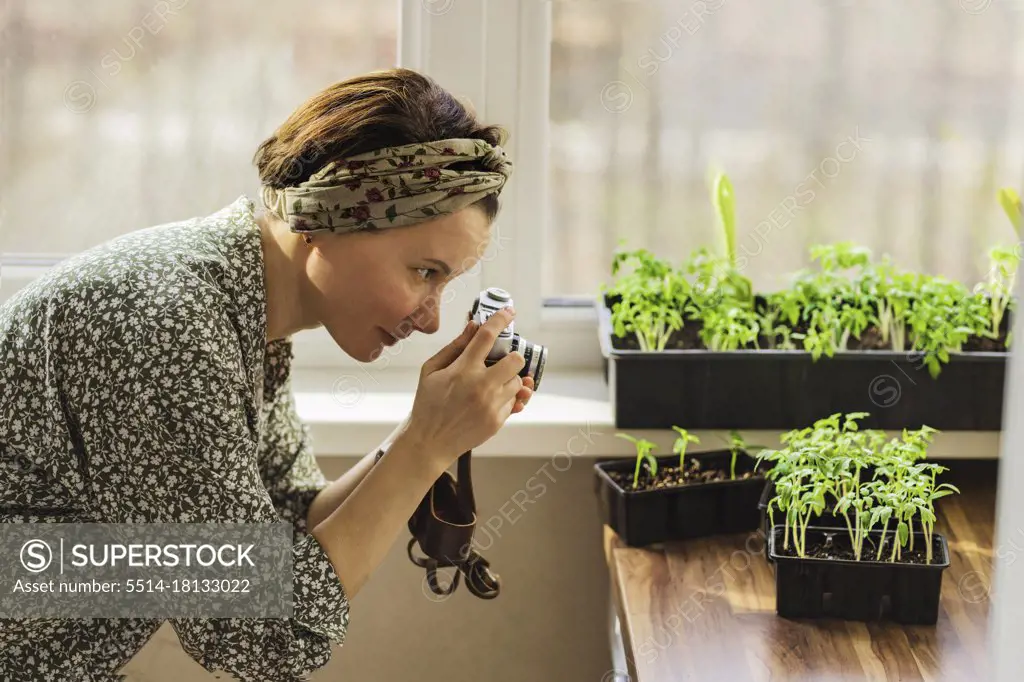 A woman takes pictures with a retro camera of the plants that she has grown in her home garden for her blog.