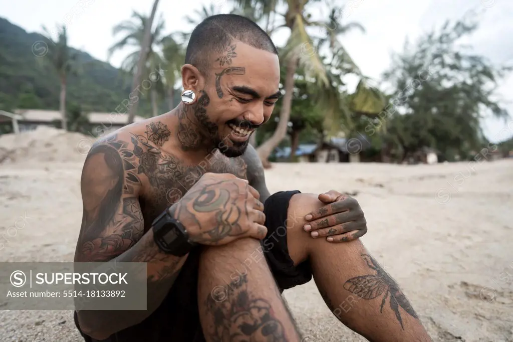 hipster guy with tattoo sitting on the beach in thailand