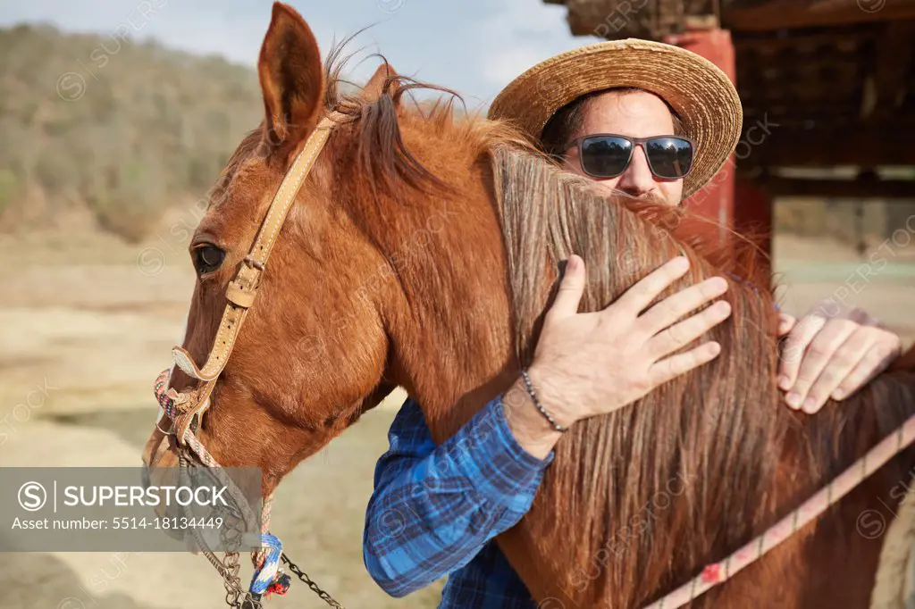 young man hat and beard hugging his horse in the field