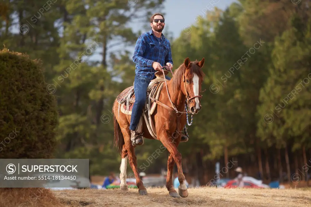 young bearded man riding his horse in the field
