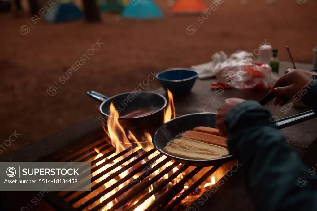 unrecognizable person preparing dinner at the campfire near his tent
