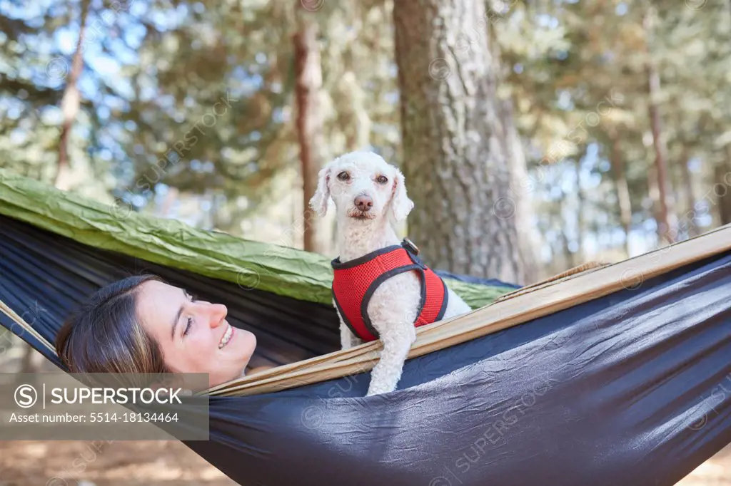 Portrait of a woman relaxing in a blue hammock with her dog in the for