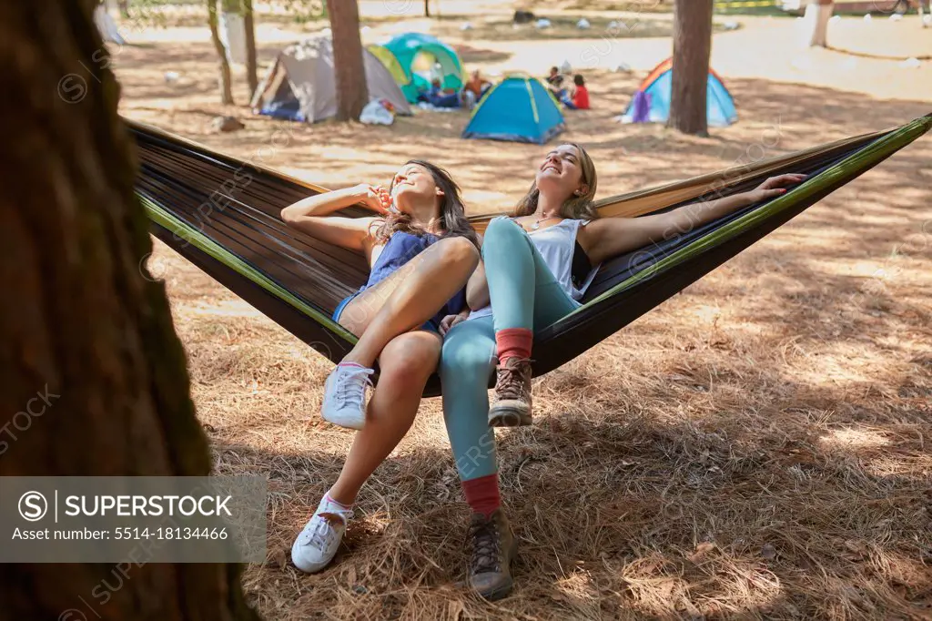 two friends having a nice time in their hammock next to their campsite