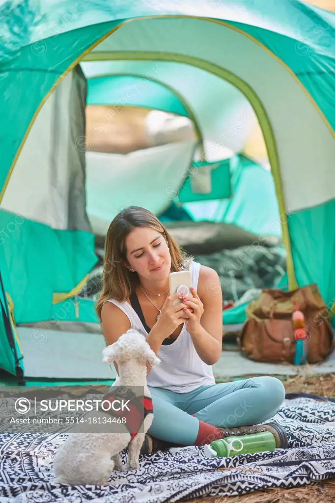 woman using her smartphone in the company of her dog outside her tent