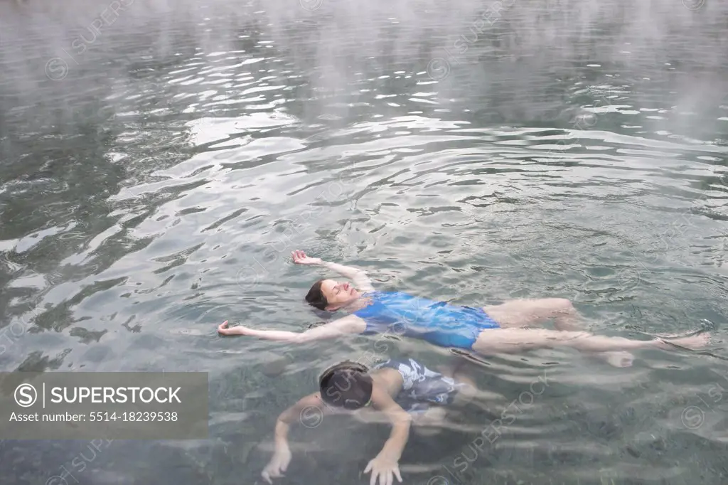 A mother and son float in Trinity Hot Springs pool with steam rising