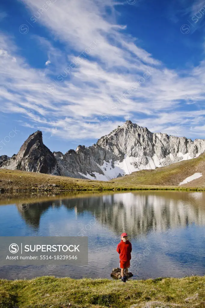Young boy wearing red, standing in front of alpine lake, scenic peaks