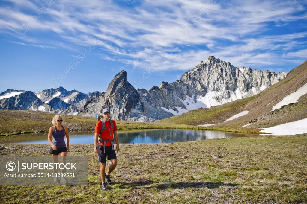 couple backpacking in scenic alpine meadow, mountains behind.