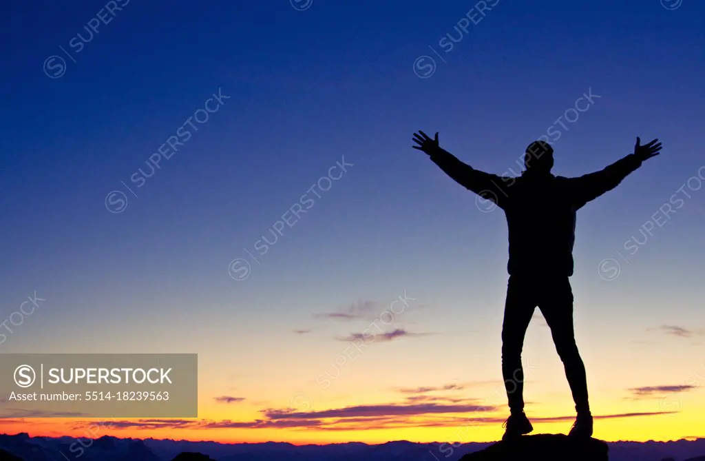 Silhouetted hiker standing on mountain summit with arms raised