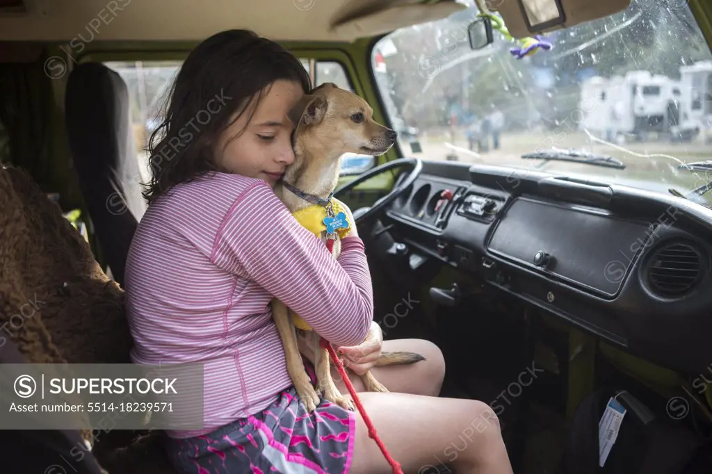 A girl hugs a chihuahua dog in VW camper van during roadtrip