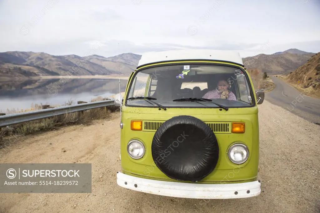 A woman and her dog are visible through windshield of VW camper van