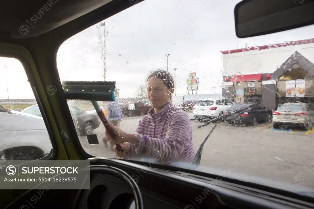 A woman cleans the windshield of VW camper van during roadtrip