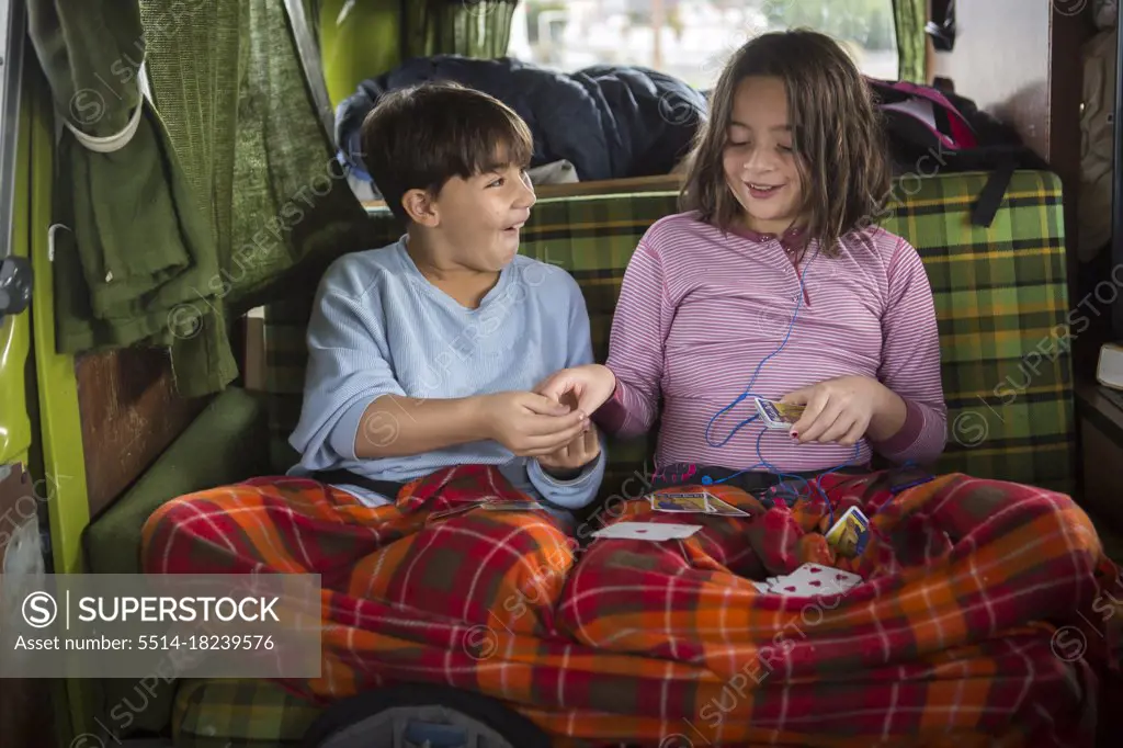 Brother and sister play cards in back of VW camper van during roadtrip