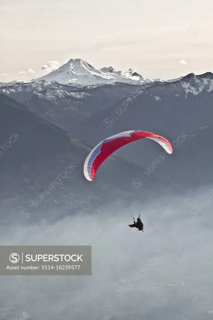 Silhouetted Paraglider sails through the air near Mount Baker.