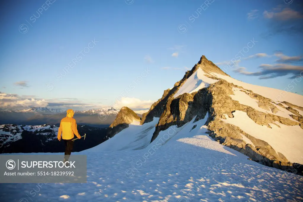 Mountaineer holding ice axe approaches mountain summit.