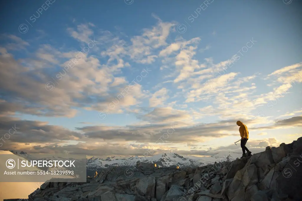 Mountaineer holding ice axe navigates a rocky mountain ridge.