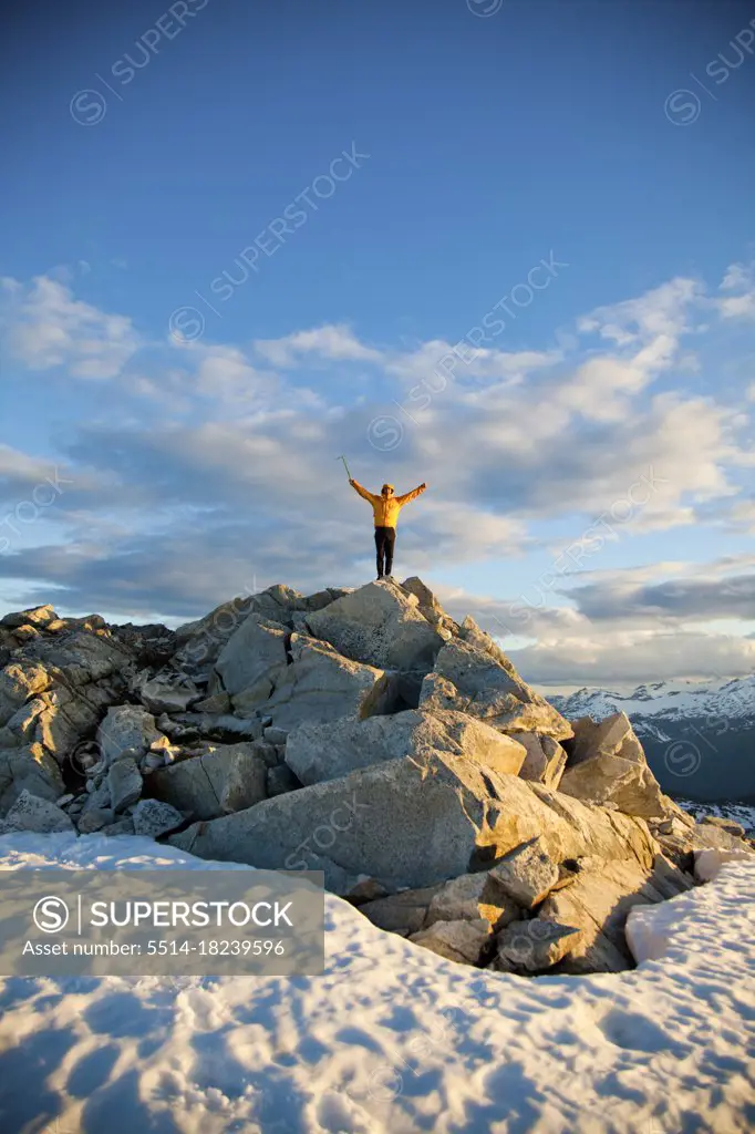 Mountaineer raises arms after a successful climb to top of mountain.