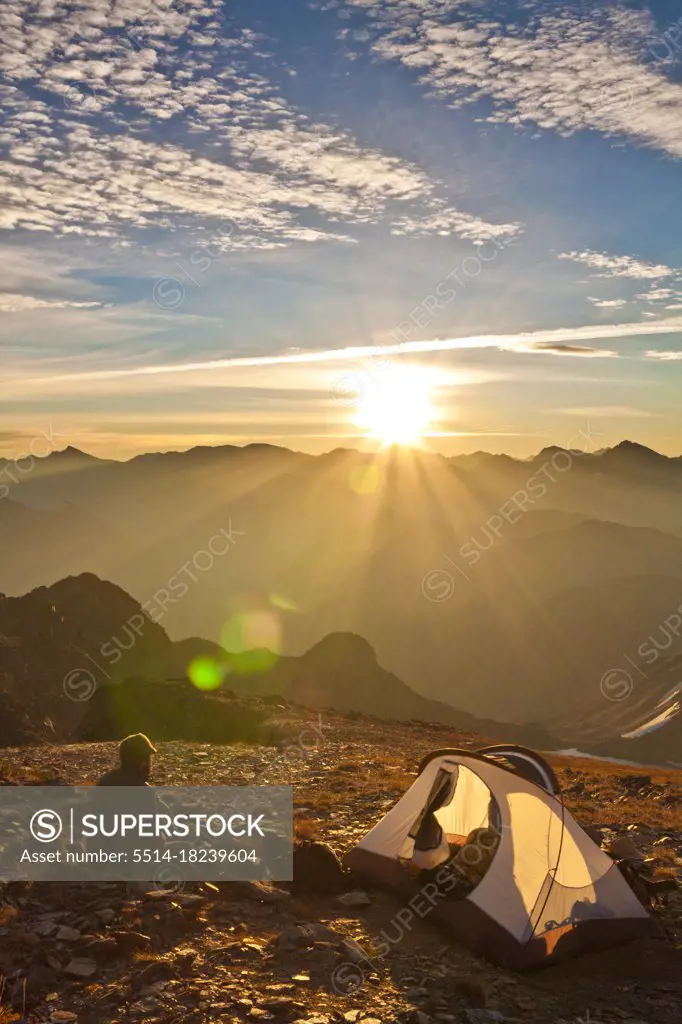 A hiker takes in the sunrise from his campsite on the summit of a mountain