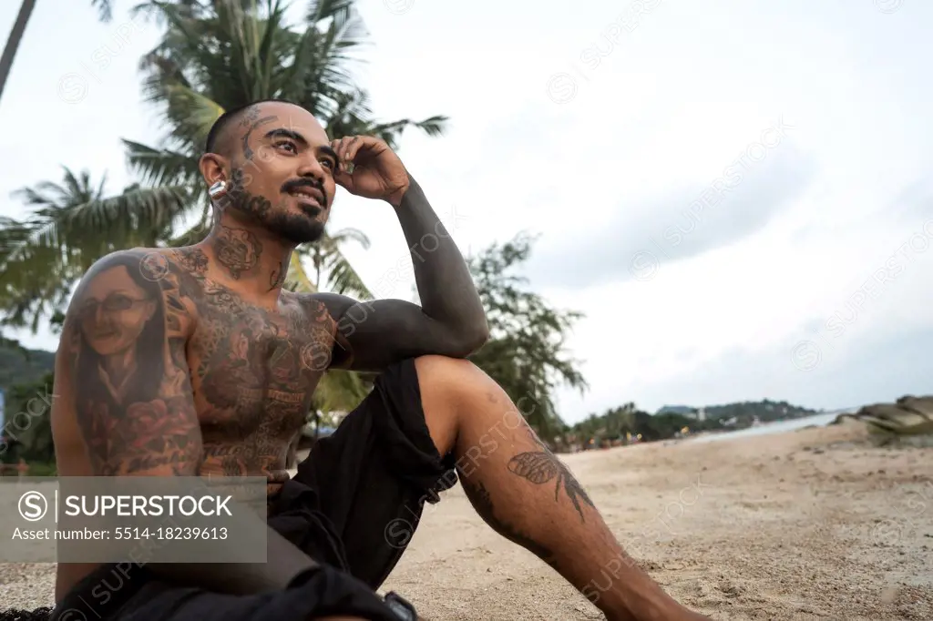 Thai guy on the seashore among the palm trees all in tattoos