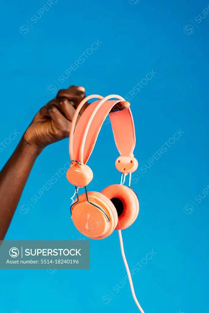 Hand of anonymous woman holding orange headphones on blue background