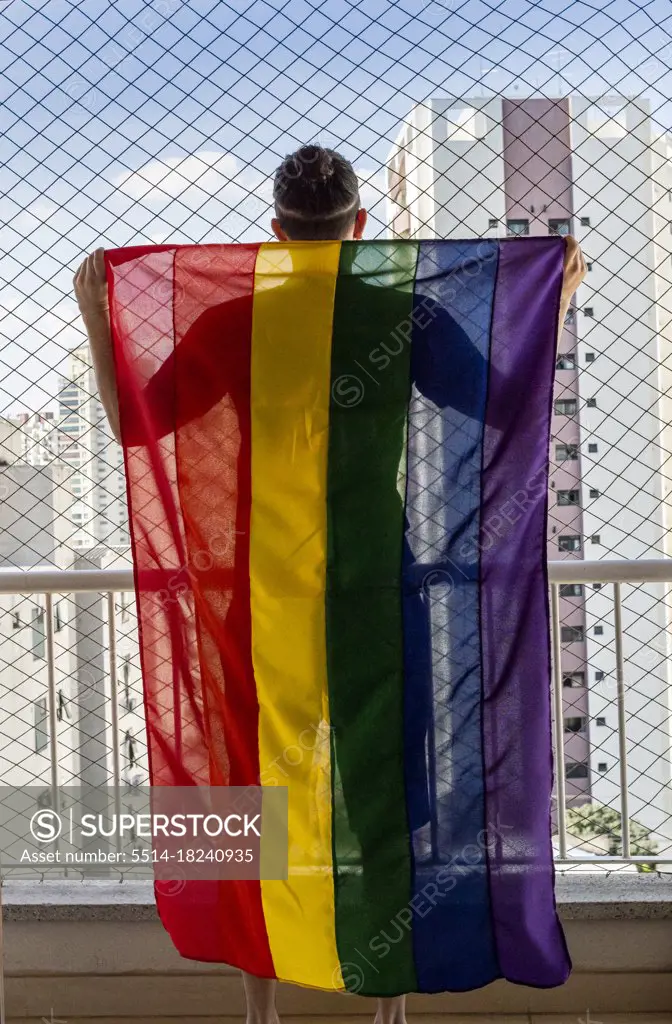 Gay man holding the rainbow flag symbol of gay pride on a balcon