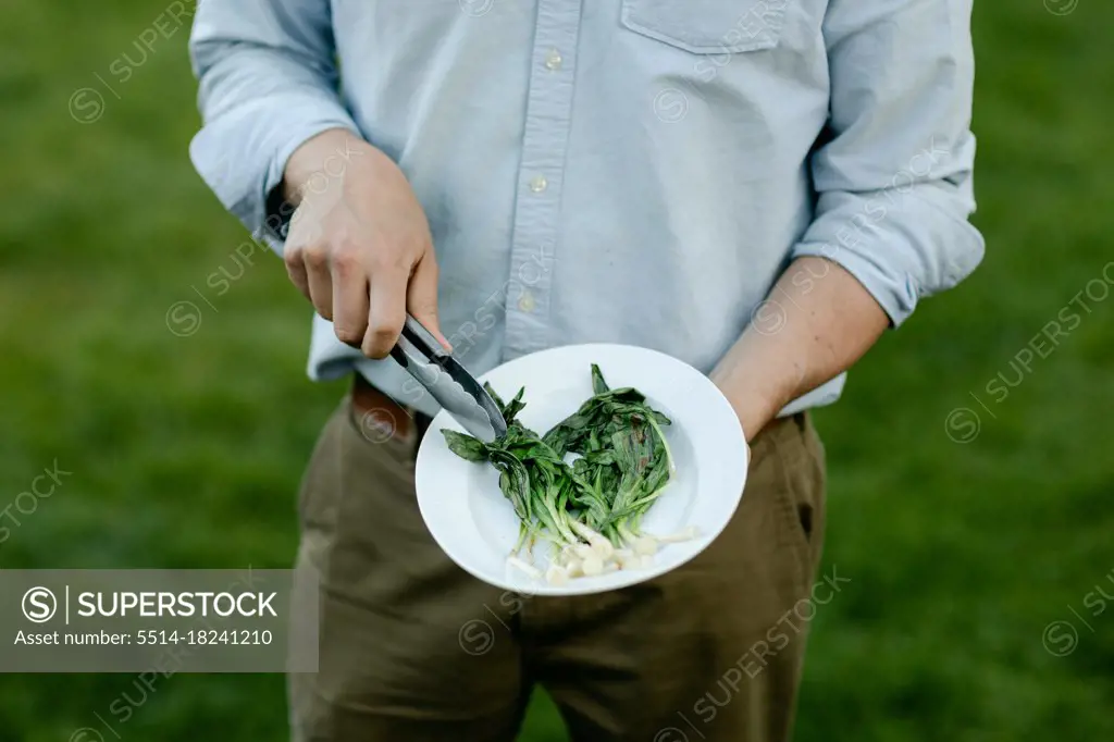 Man's hands holding a platter of grilled and wilted ramps