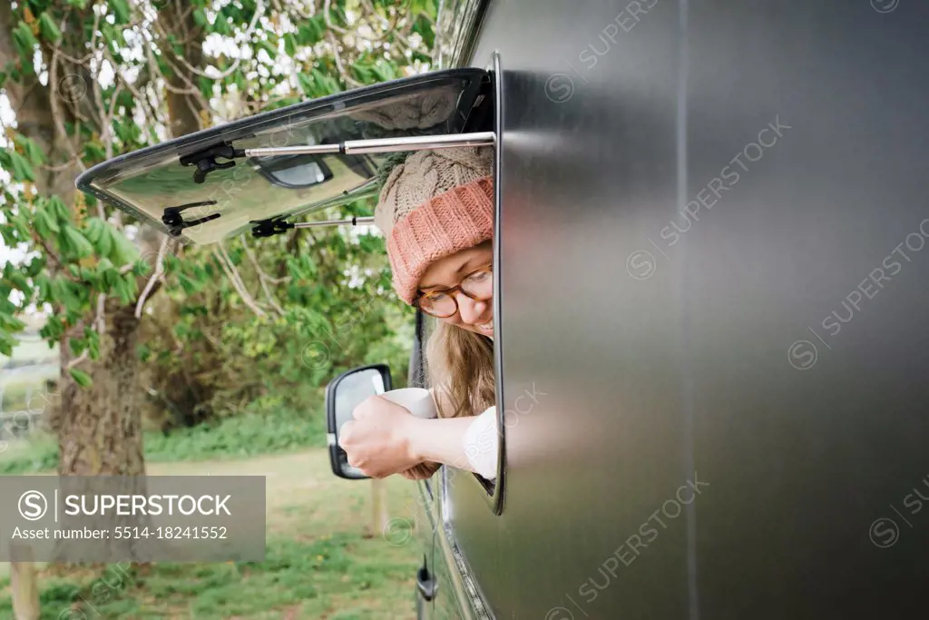 woman looking out of her camper window smiling enjoying a cup of tea
