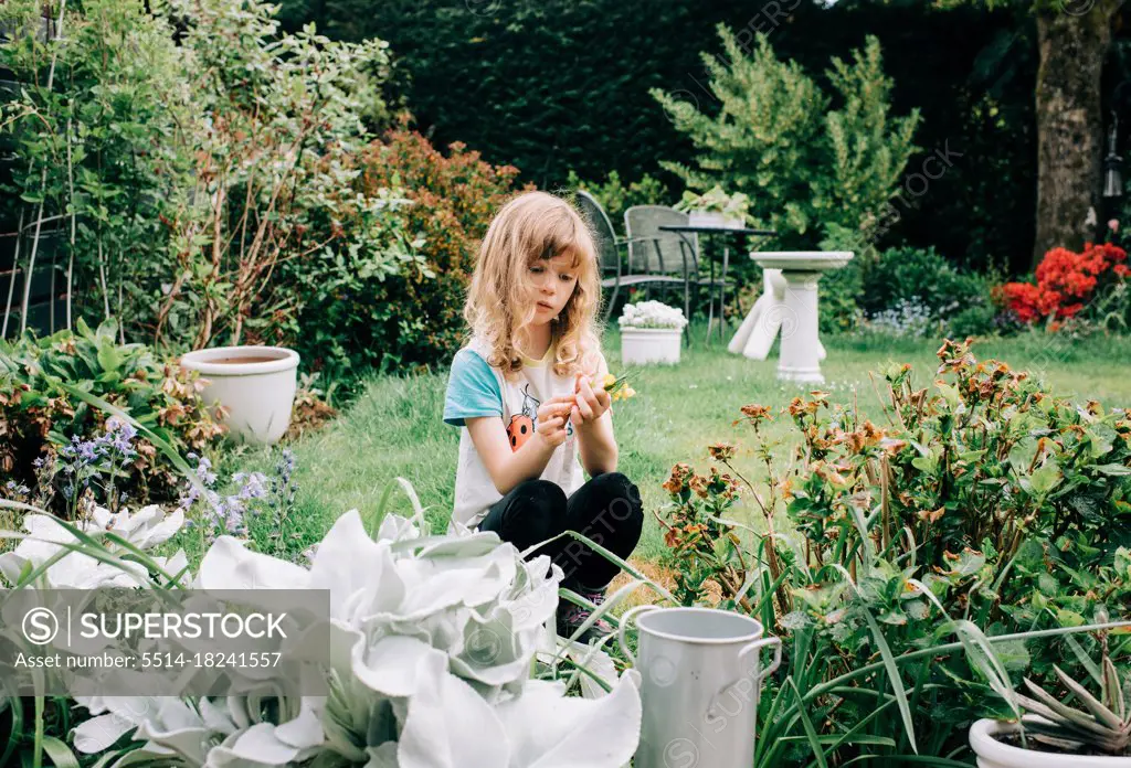 girl sat in a beautiful back yard picking flowers looking thoughtful