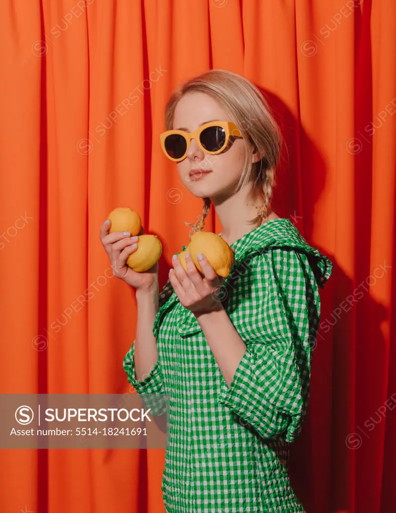 Style woman in green dress and sunglasses with lemons on orange
