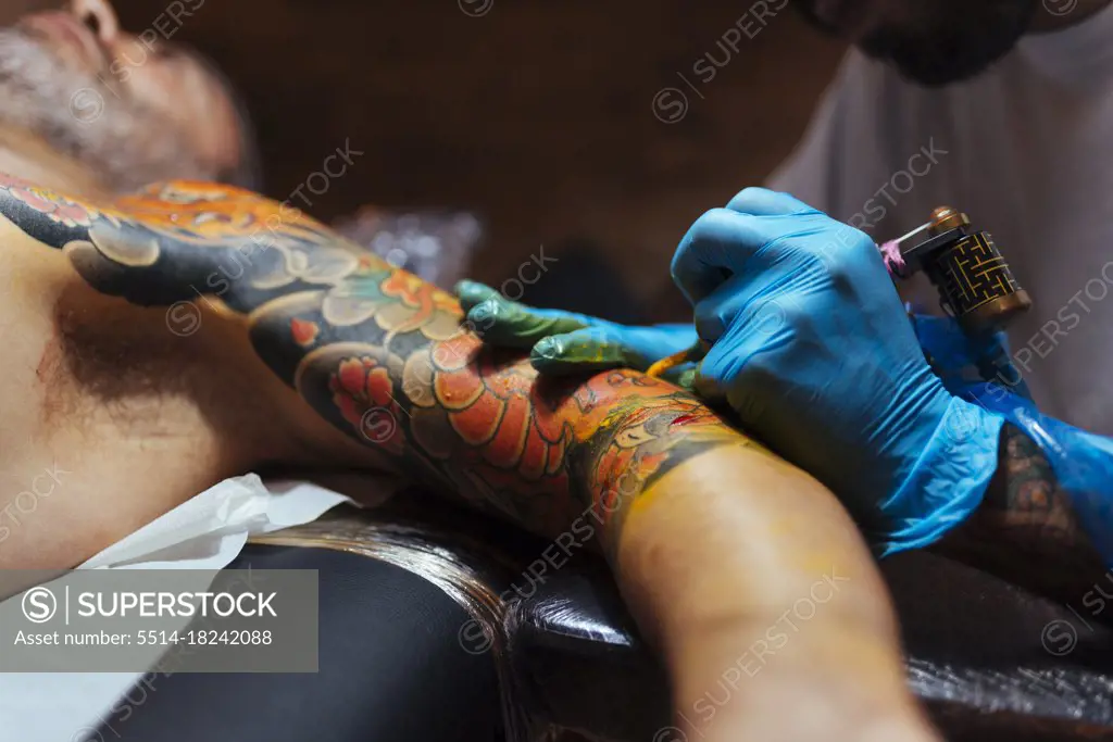 Close up of hands of an artist tattooing on a customer's arm.