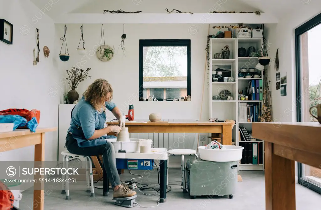 woman spinning clay on a pottery wheel in her home studio office in UK