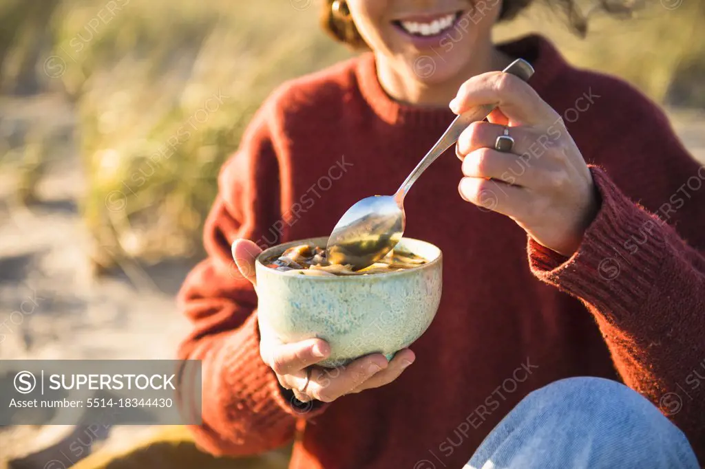 Young woman enjoying soup while beach car camping alone