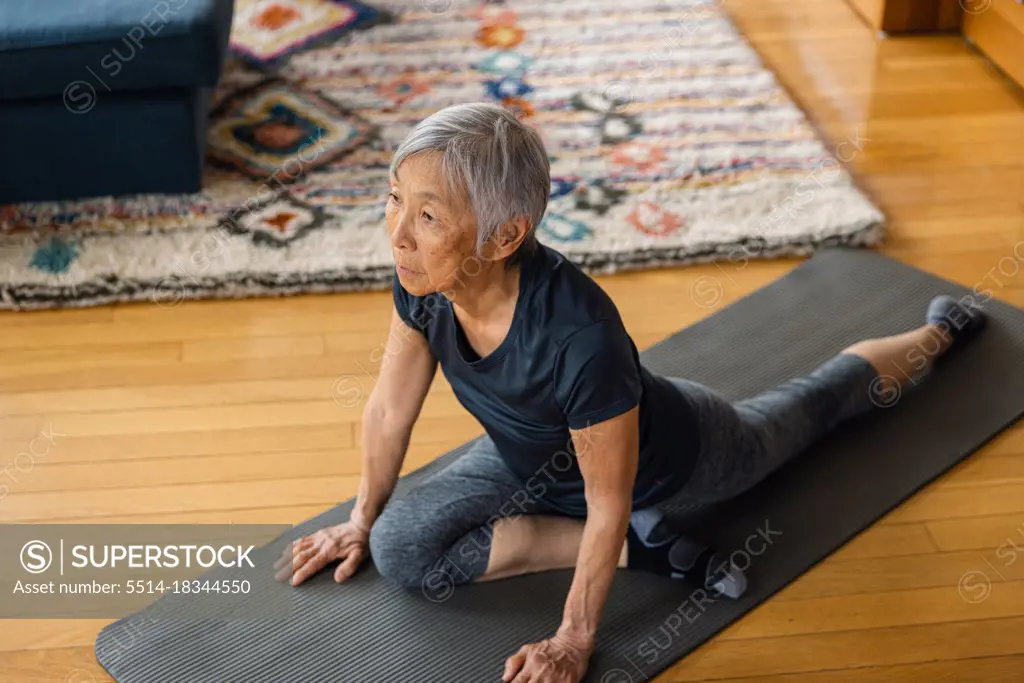 Senior asian woman stretching on exercise mat in living room