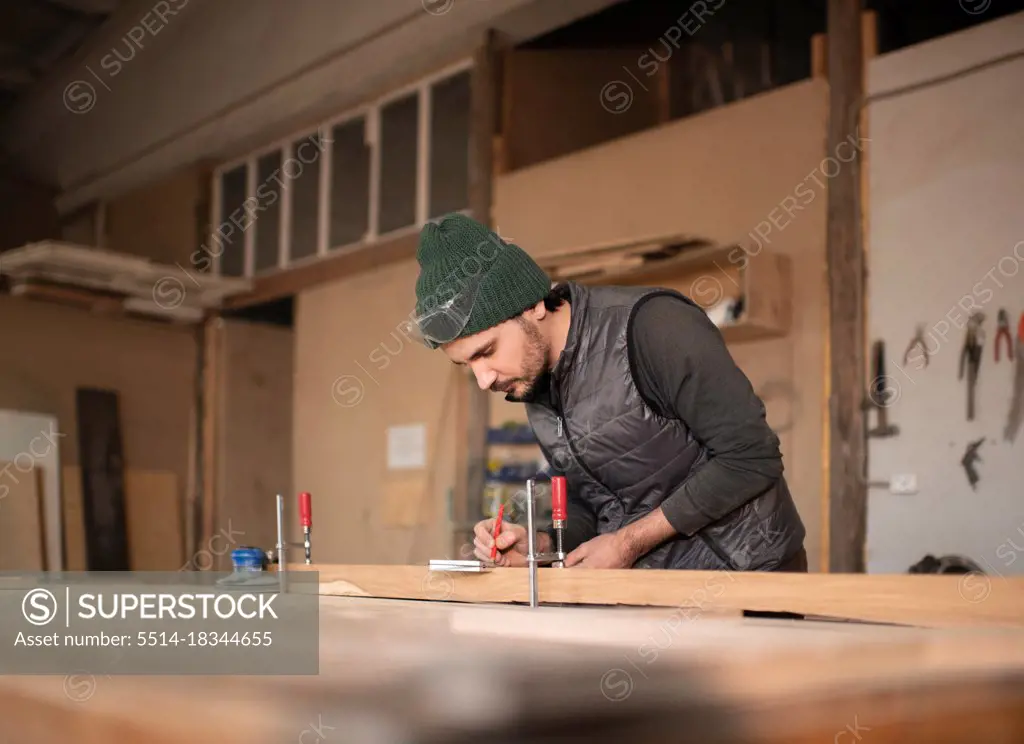 Male carpenter making marks on plank