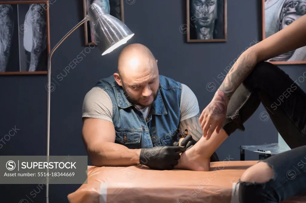 Bald man making tattoo on foot of woman