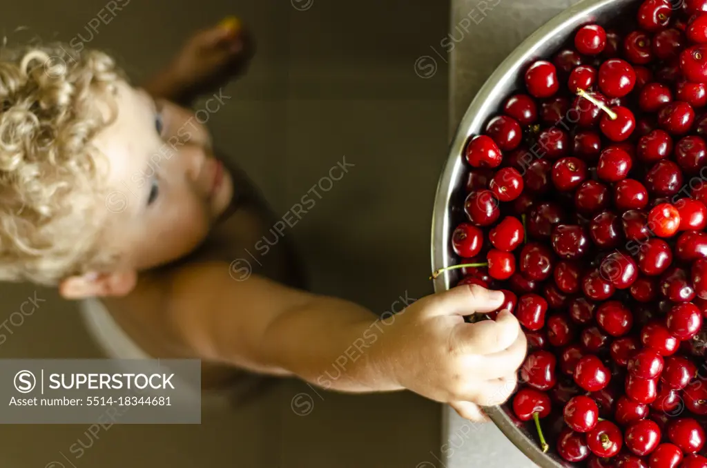 boy 2 years old reaching for a cherry, top view