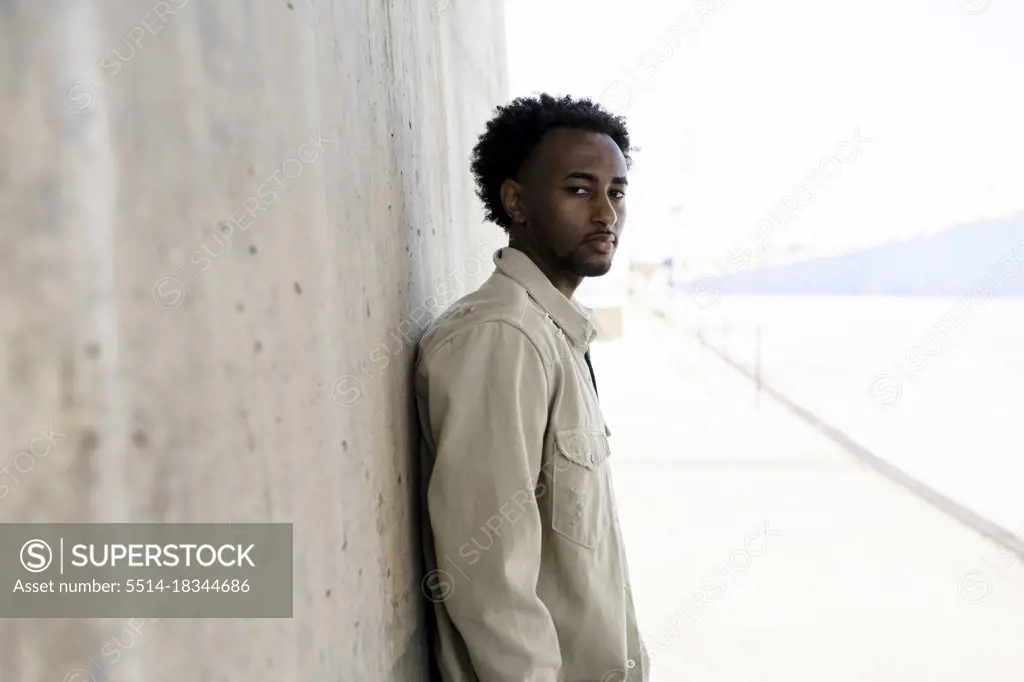 Black man leaning on concrete wall with hands on pocket