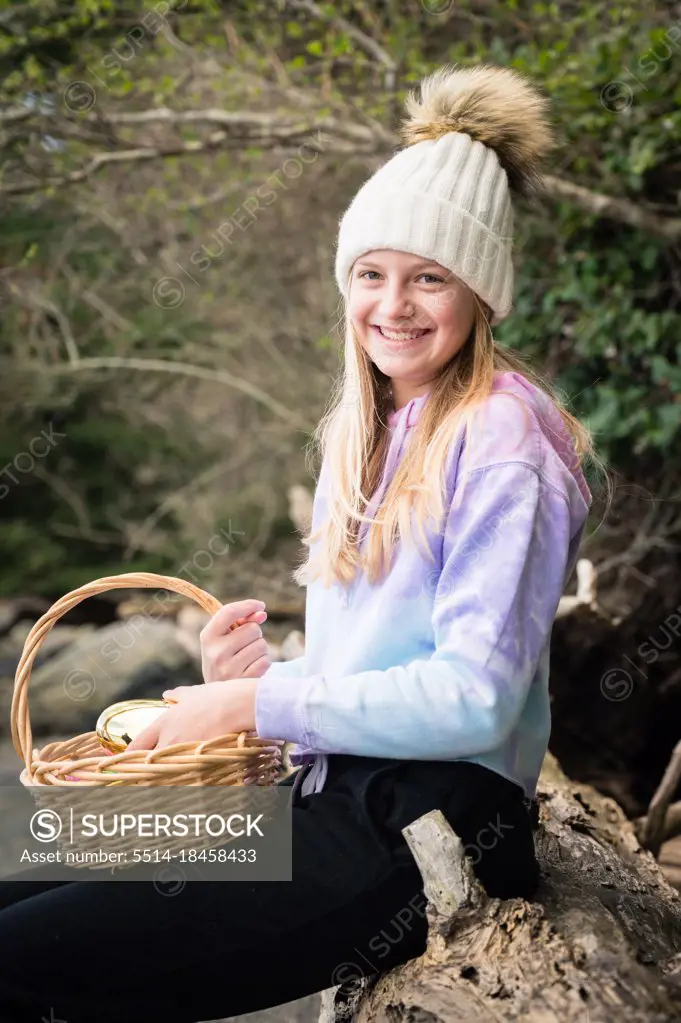 Teen Girl in Winter Hat Sitting on Log Holding Easter Basket