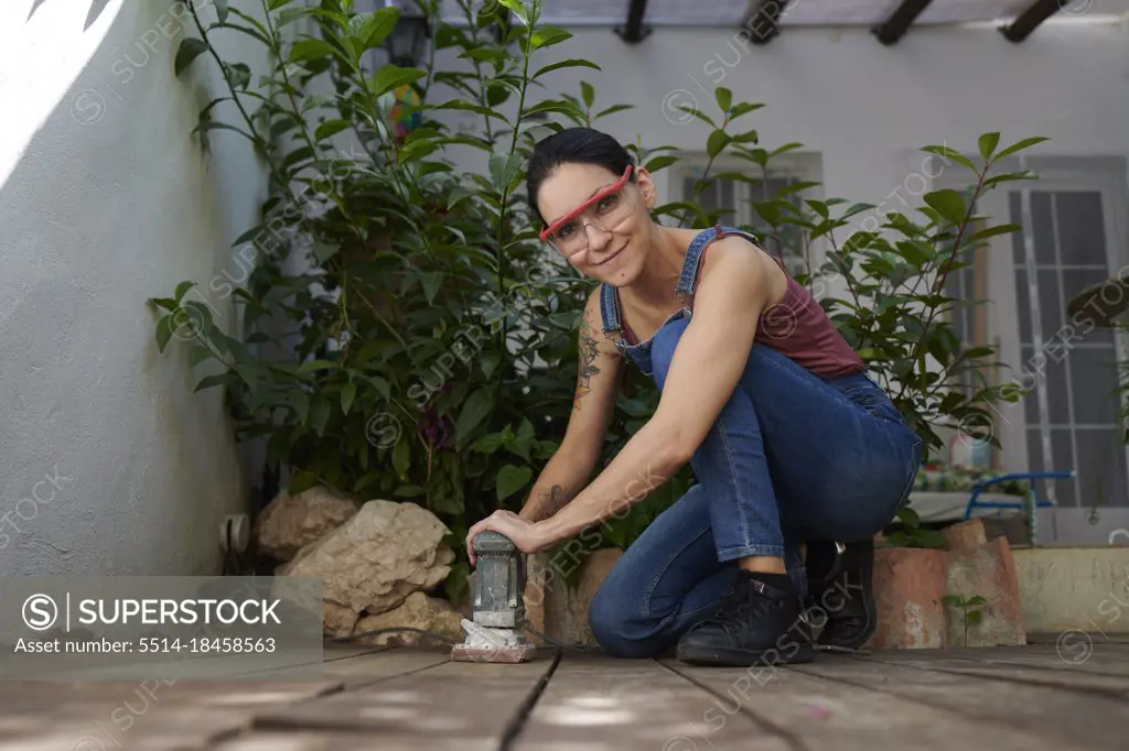 A woman wearing safety goggles looks at the camera for woodworking.