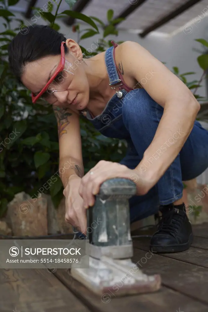 a young woman wearing safety goggles sanding the wood on the floor