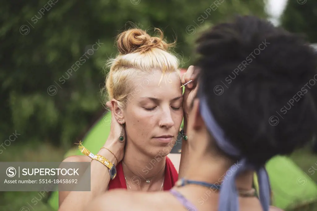 queer women paint golden facepaint at campsite for festival