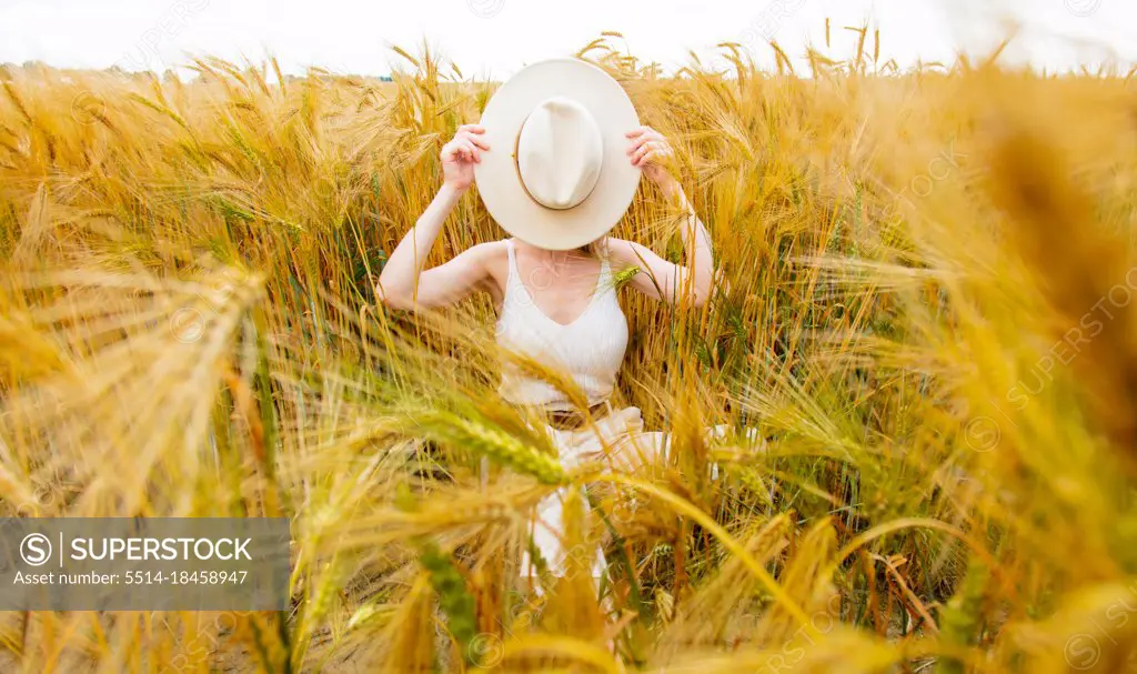 Woman with a blond hair and white hat sit in golden wheat field