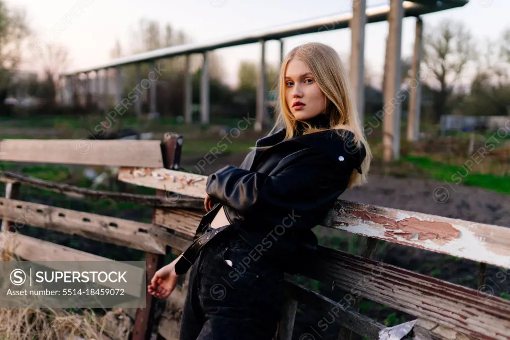 Stylish blonde woman standing near a wooden fence in a leather jacket